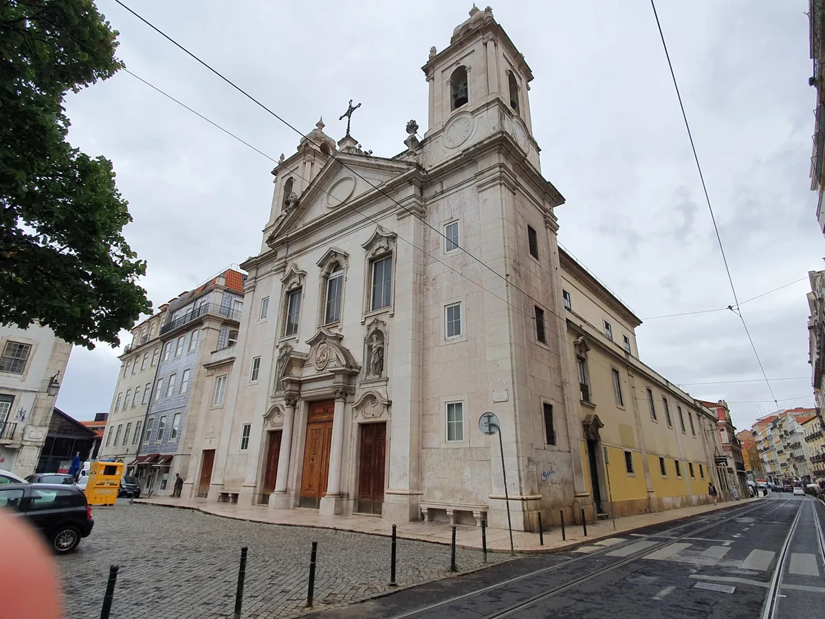 Kostel svatého Pavla pohledem z rohu jeho náměstí, jedna zvonice se tyčí nad bledě kamenným průčelím, žlutá boční zeď běží podél ulice